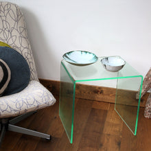 Glass effect acrylic side table with two bowls on a wooden floor next to a patterned chair.